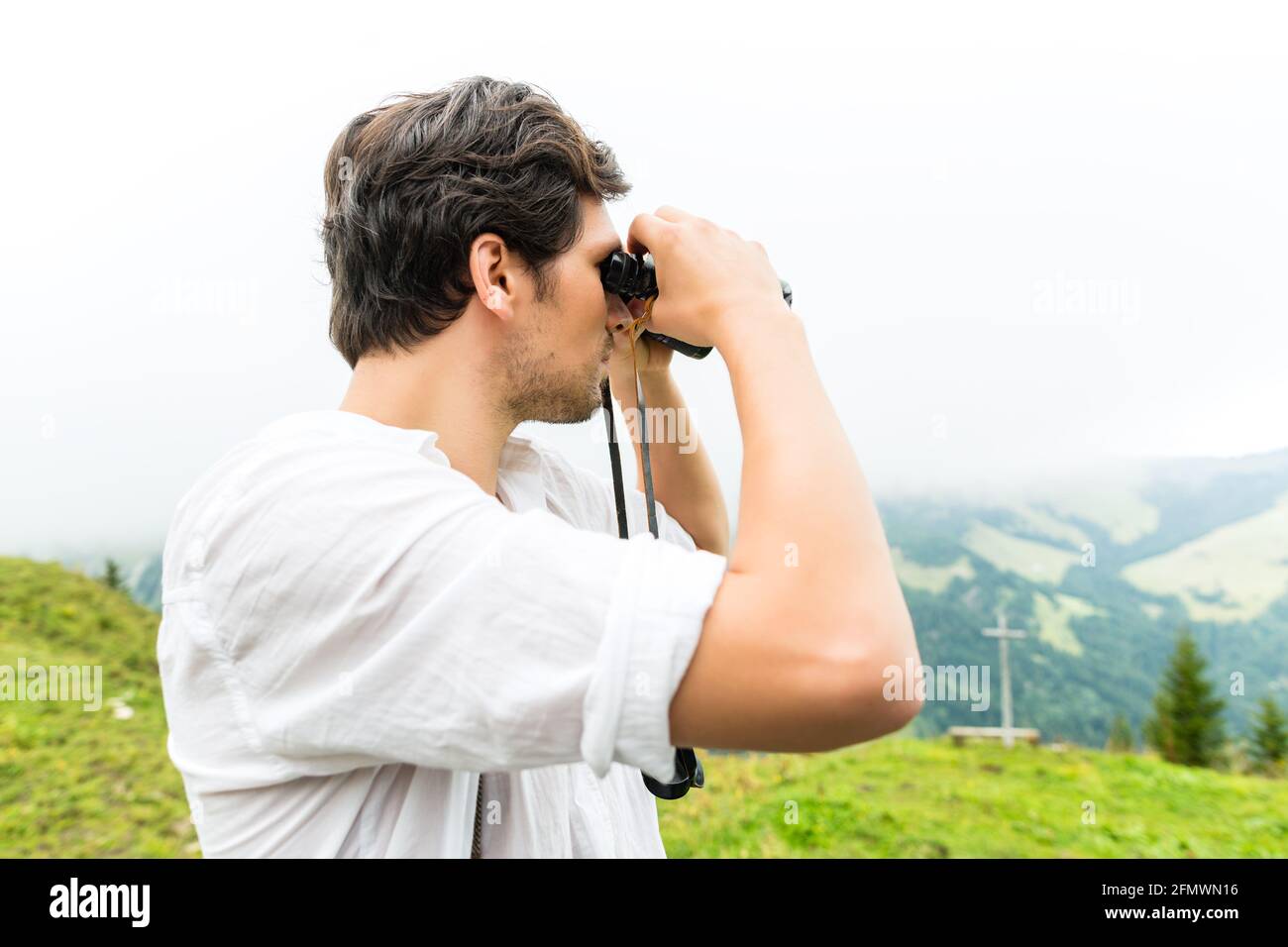 Hiking - Young man in the Bavarian Alps looking through a field glasses or binocular enjoying the panorama in the leisure time or vacation Stock Photo