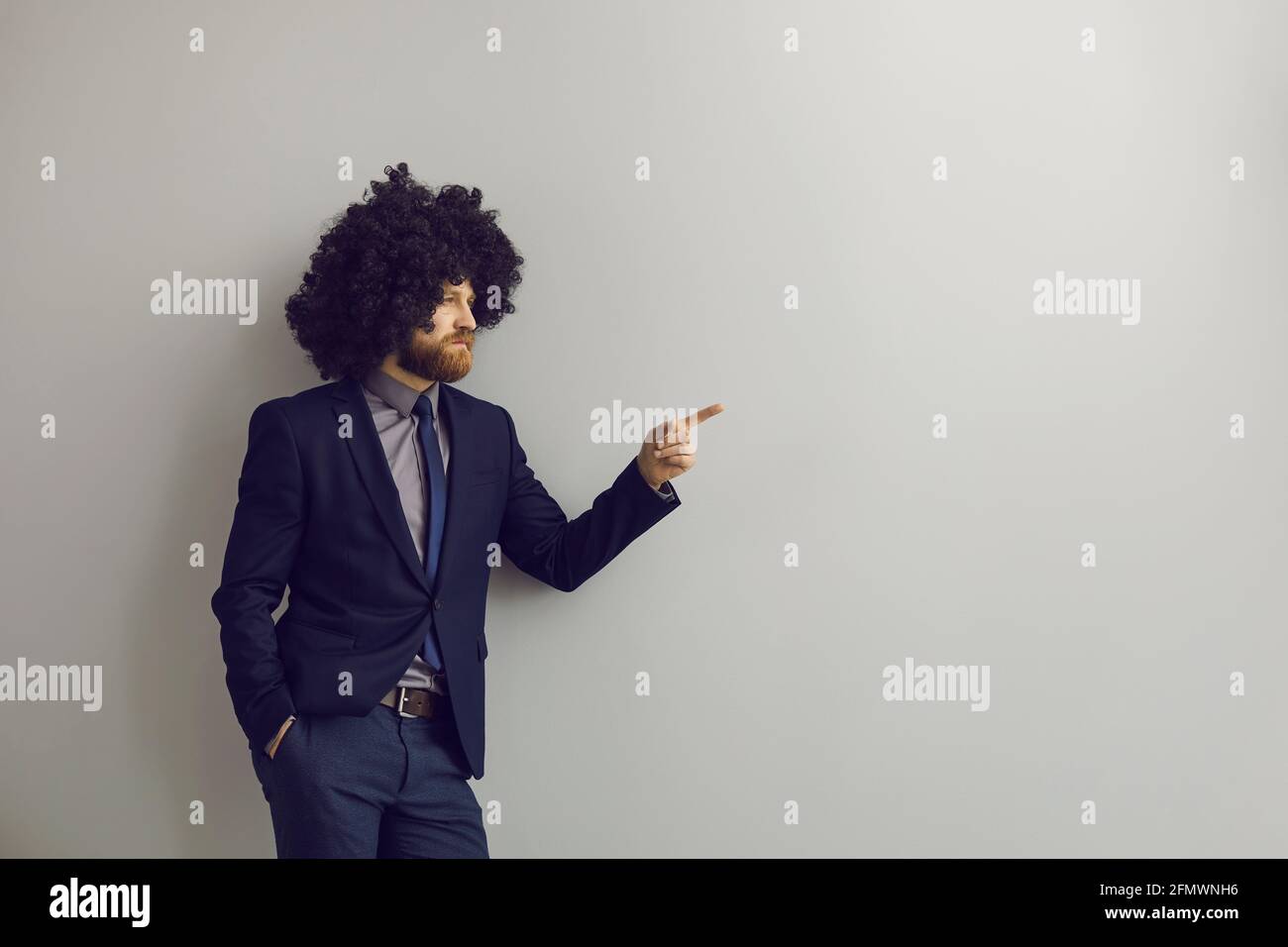Serious businessman leaning on wall and pointing finger away at advertising copy space Stock Photo
