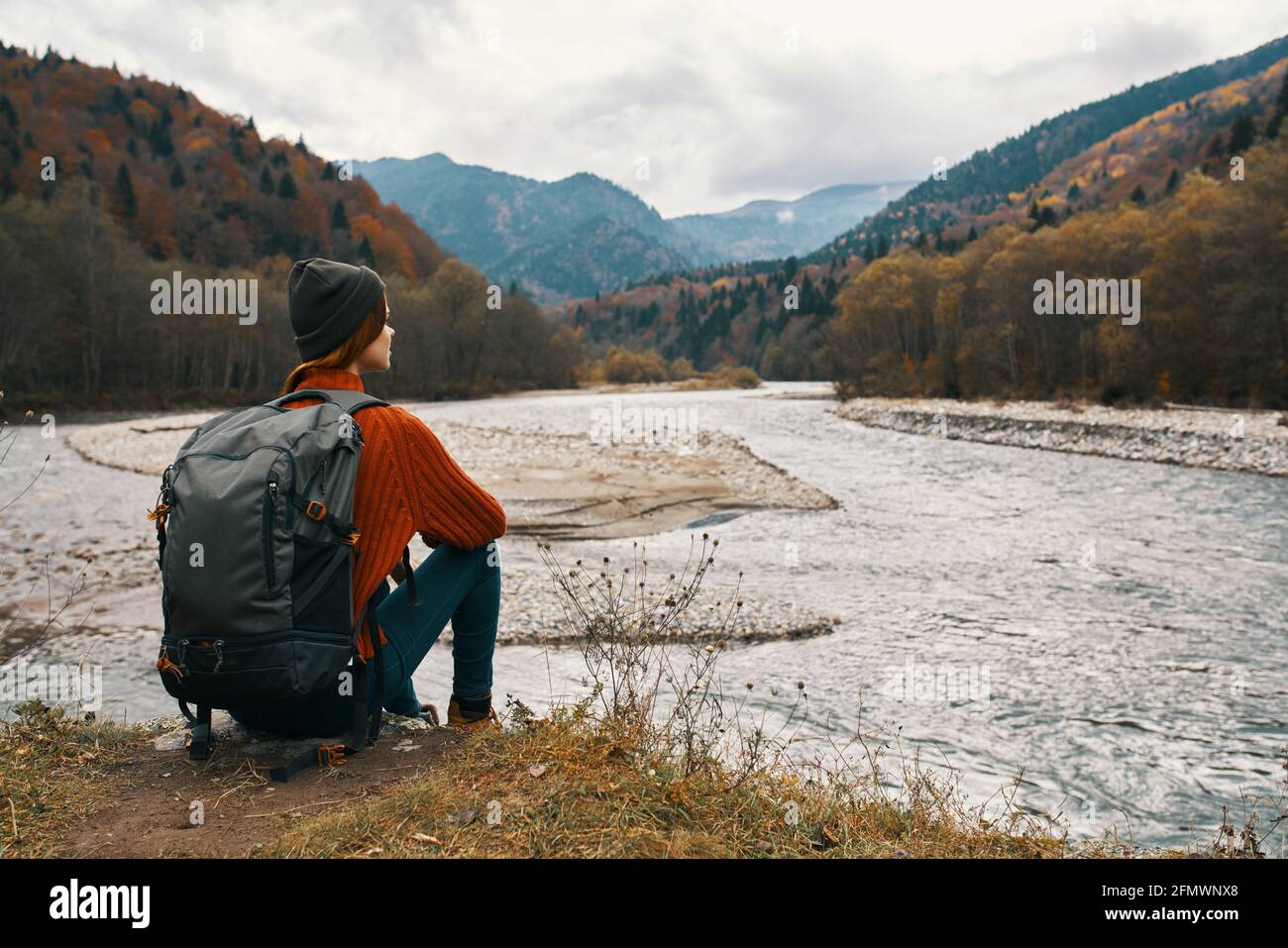 woman with a backpack in a jacket and a hat on the river bank in the ...