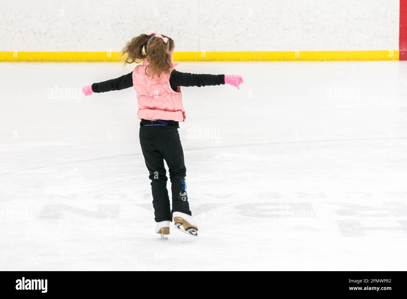 Little girl practicing figure skating moves on the indoor ice rink ...