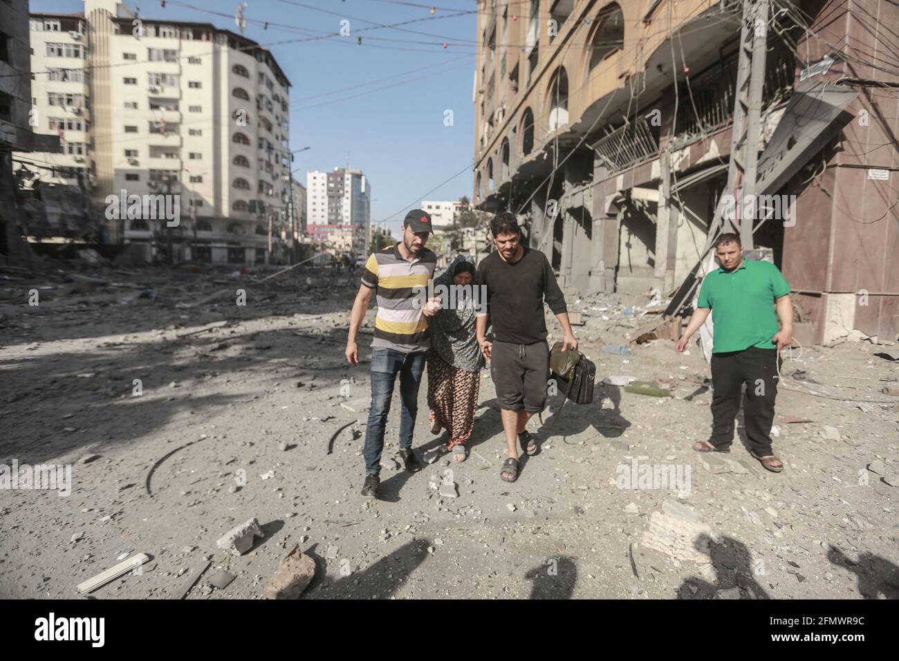 Gaza City, Palestinian Territories. 12th May, 2021. People walk past the rubble near the severely damaged Al-Jawhara Tower in Gaza City after it was hit by Israeli airstrikes amid the escalating flare-up of Israeli-Palestinian violence. The Health Ministry in the Hamas-run Gaza Strip said the number of Palestinians killed has risen to 35, including 12 children, while 233 people were reported injured. Credit: Mohammed Talatene/dpa/Alamy Live News Stock Photo