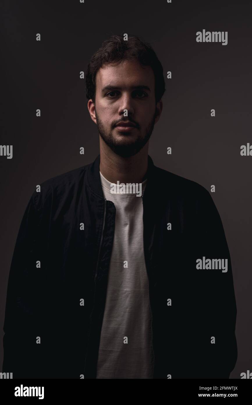 Vertical shot of a bearded Caucasian man with minimalist clothing against a black background Stock Photo