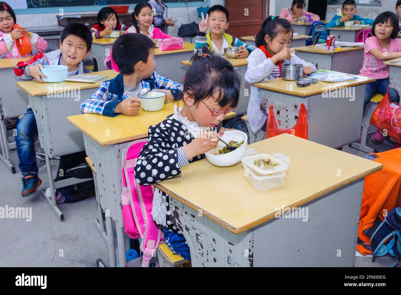 Students from Weiqiao Central Primary School in Xiuning, Anhui, China eating lunch in their classroom. Stock Photo