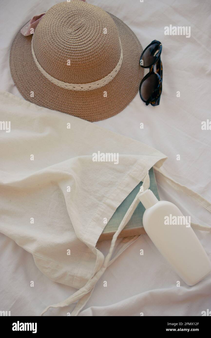 Vertical image of a hat, sun cream, a closed book and sunglasses. Perfect outfit to enjoy the summer. Summer Concept 2021. Stock Photo