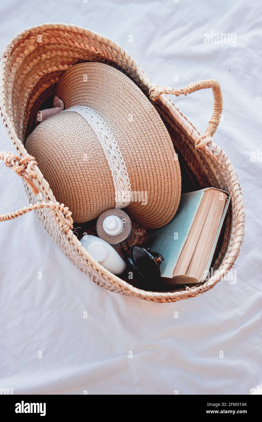 Top View vertical pho of a summer bag with sun cream, a book and sunglasses on it. Perfect set to enjoy a sunny day at the beach. Summer Concept 2021. Stock Photo