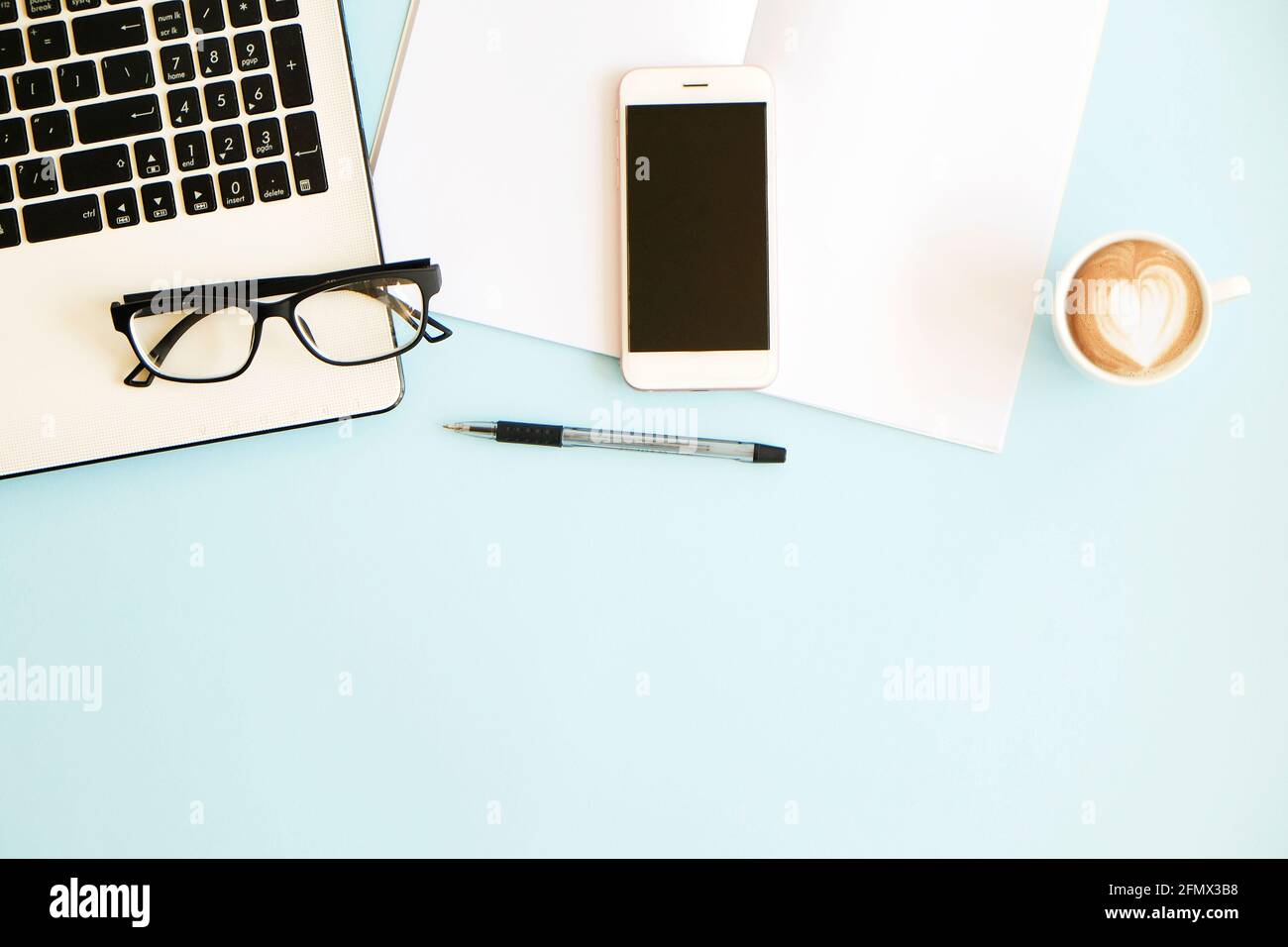 Minimalistic flat lay composition of black & white laptop computer keyboard, cell phone gadget, cup of coffee & folded glasses on blue surface desk ta Stock Photo