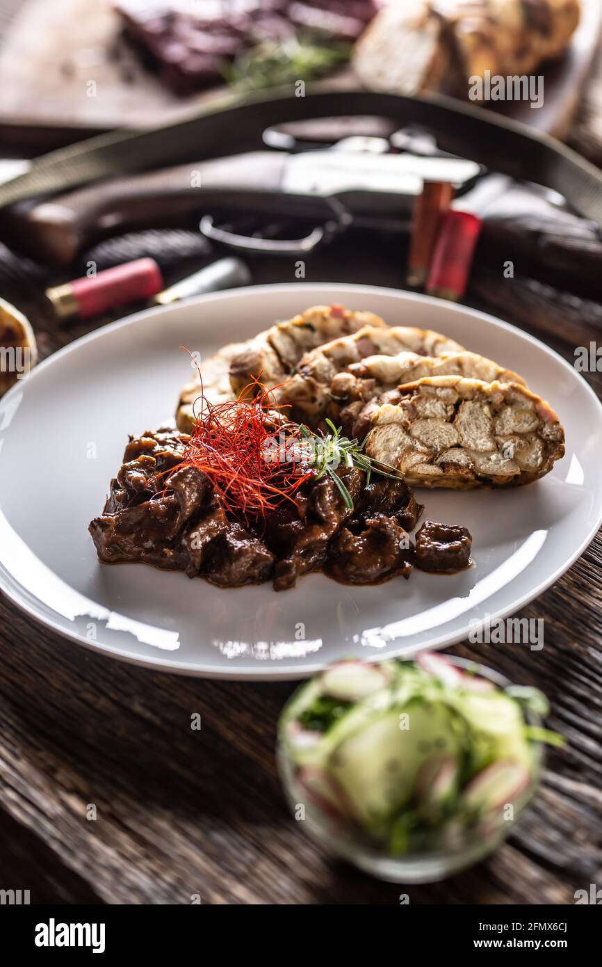 Porcelain plate full of deer venison goulash stew served with dumpling and fresh salad as an appetizer. Food is surrounded by hunting accesories such Stock Photo