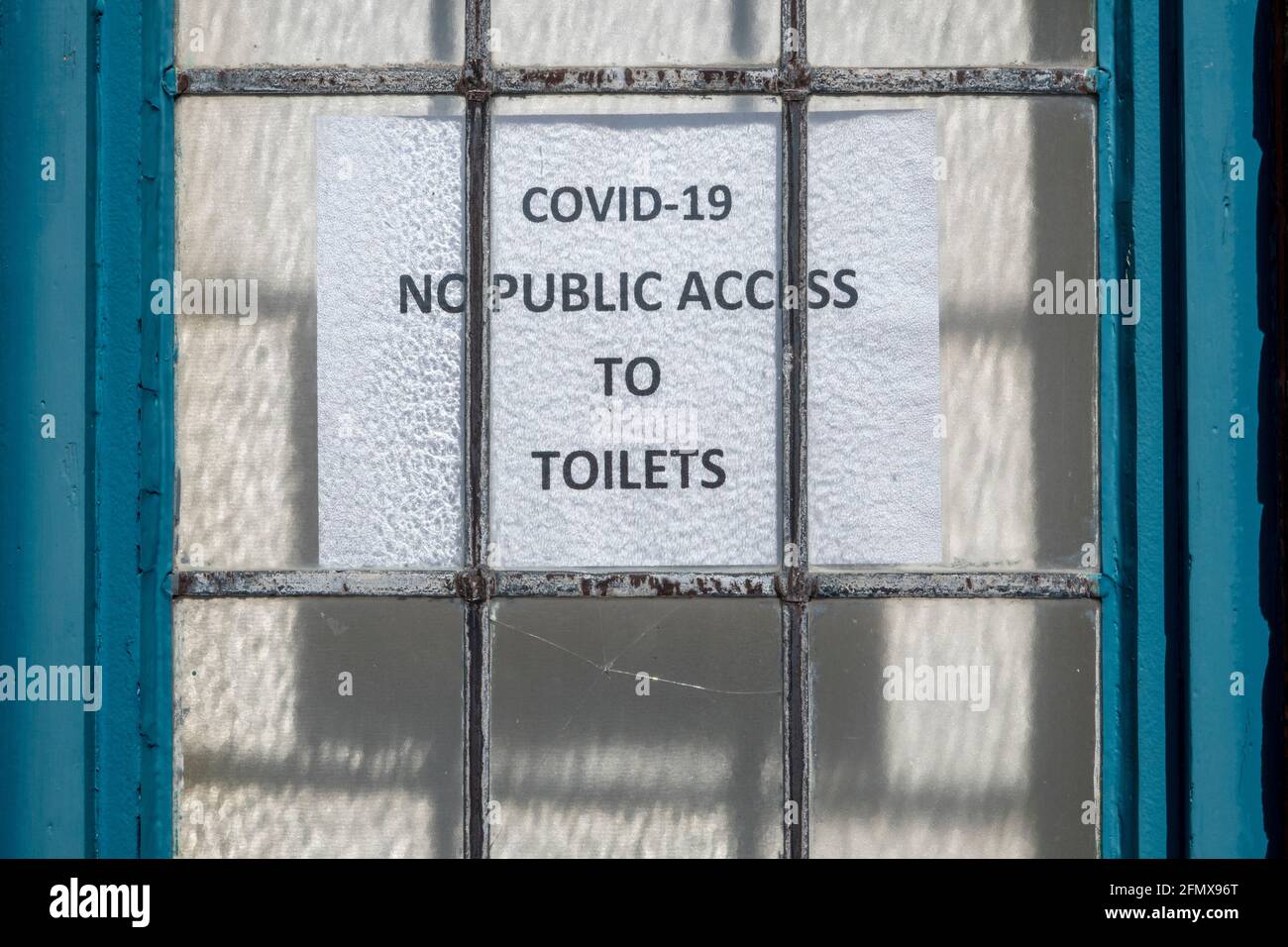 A Covid -19 'No Public Access to Toilets'  sign stuck to the back of a leaded window in a wooden frame Stock Photo