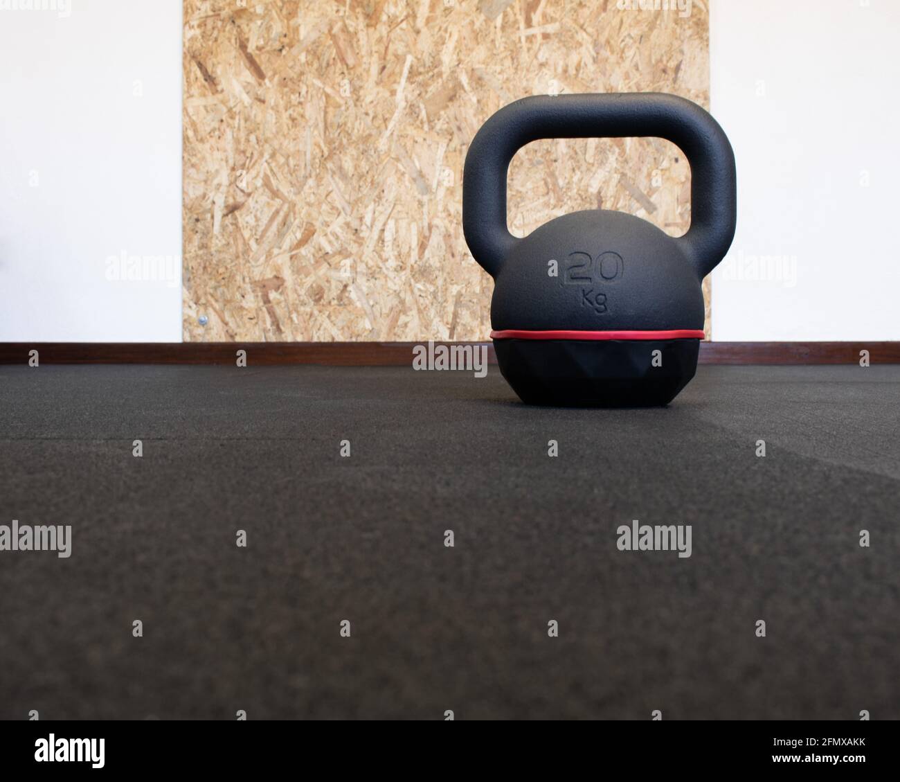 20Kg black kettlebell isolated on the floor at the gym. Bodybuilding and fitness equipment with wooden wall protection board in the background Stock Photo