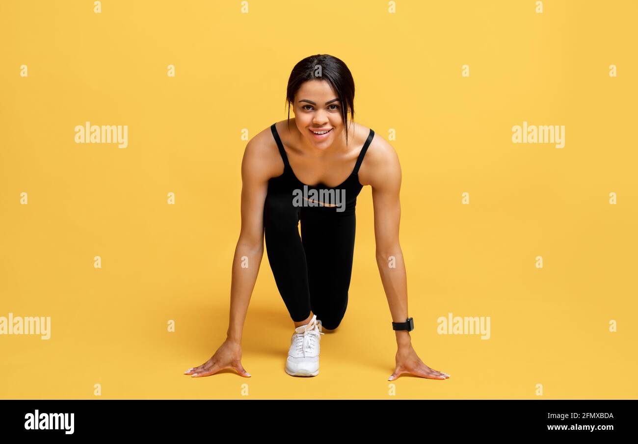Cardio training and start. Happy black woman in sports uniform ready to run, isolated on yellow background, studio shot Stock Photo