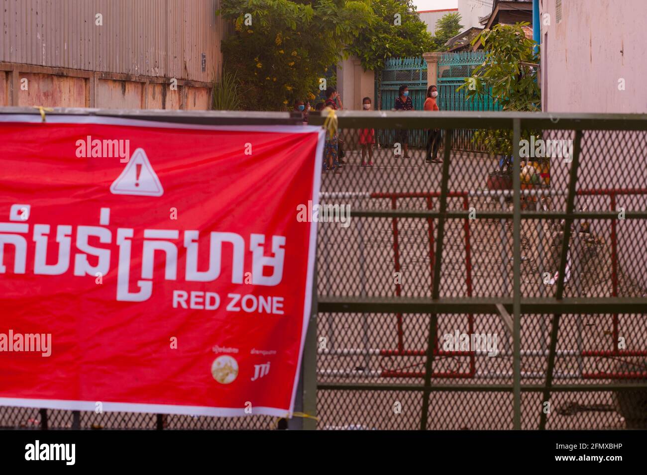 Phnom Penh, Cambodia. May 12th, 2021. after 4 weeks of the city being in total lockdown, the government has continued to divide Phnom Penh into 3 color zones (red, orange & yellow) due to the ongoing COVID - 19 surge. a Cambodian family is in quarantine behind a police checkpoint w/ a large colorful bilingual banner that lets people know this is the entrance to a 'Red Zone', meaning high risk of infection. credit: Kraig Lieb / Alamy Live News Stock Photo