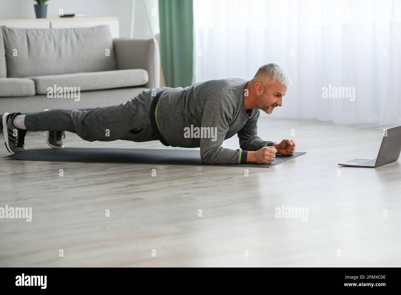 Athletic bearded older man doing exercises at home, using laptop Stock Photo