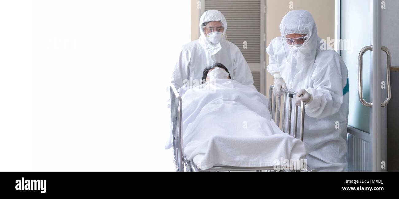asian male nurse and doctor wearing ppe suit and face mask pushing stretcher gurney bed with seriously infected coronavirus or covid-19 patient toward Stock Photo