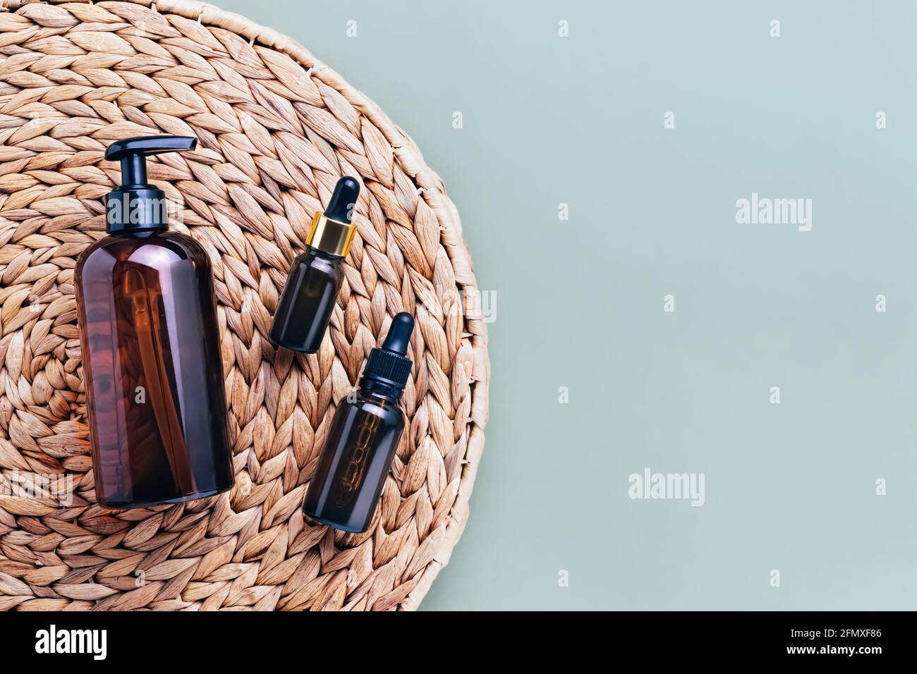 Dropper bottles of essential oil and serum, dark dispenser bottle of shower gel, on rattan background. Beauty and SPA concept. Flat lay, copy space, t Stock Photo