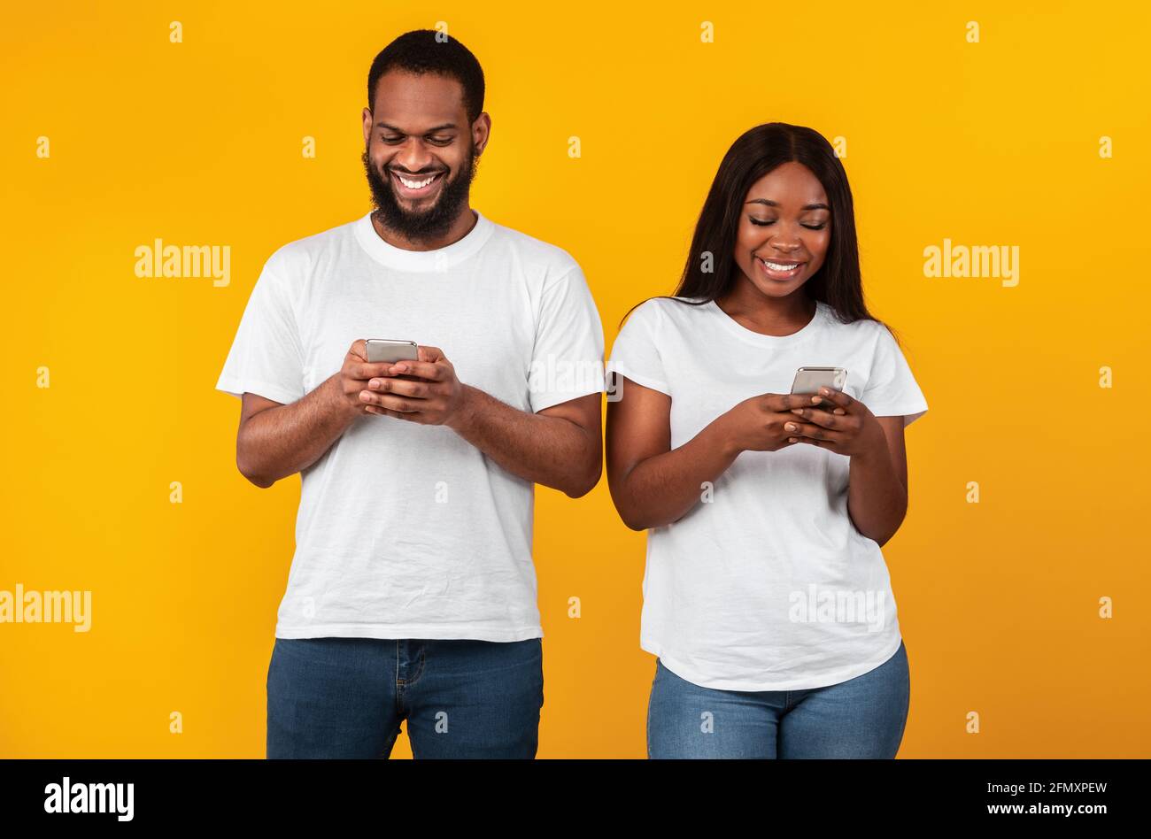 Black couple using smartphones, standing at studio Stock Photo