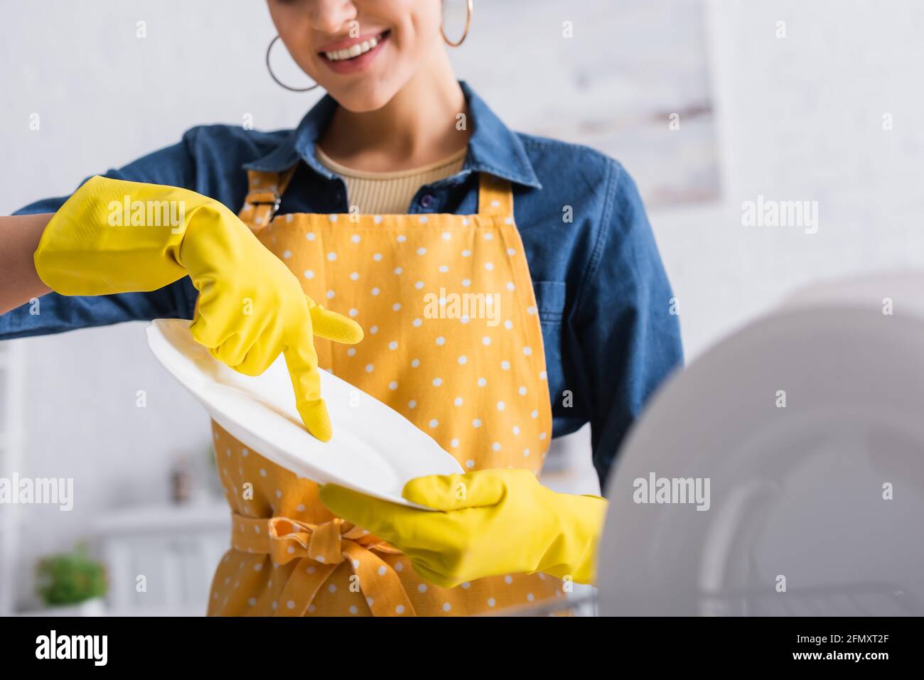 Cropped view of smiling woman in rubber gloves holding clean plate Stock Photo