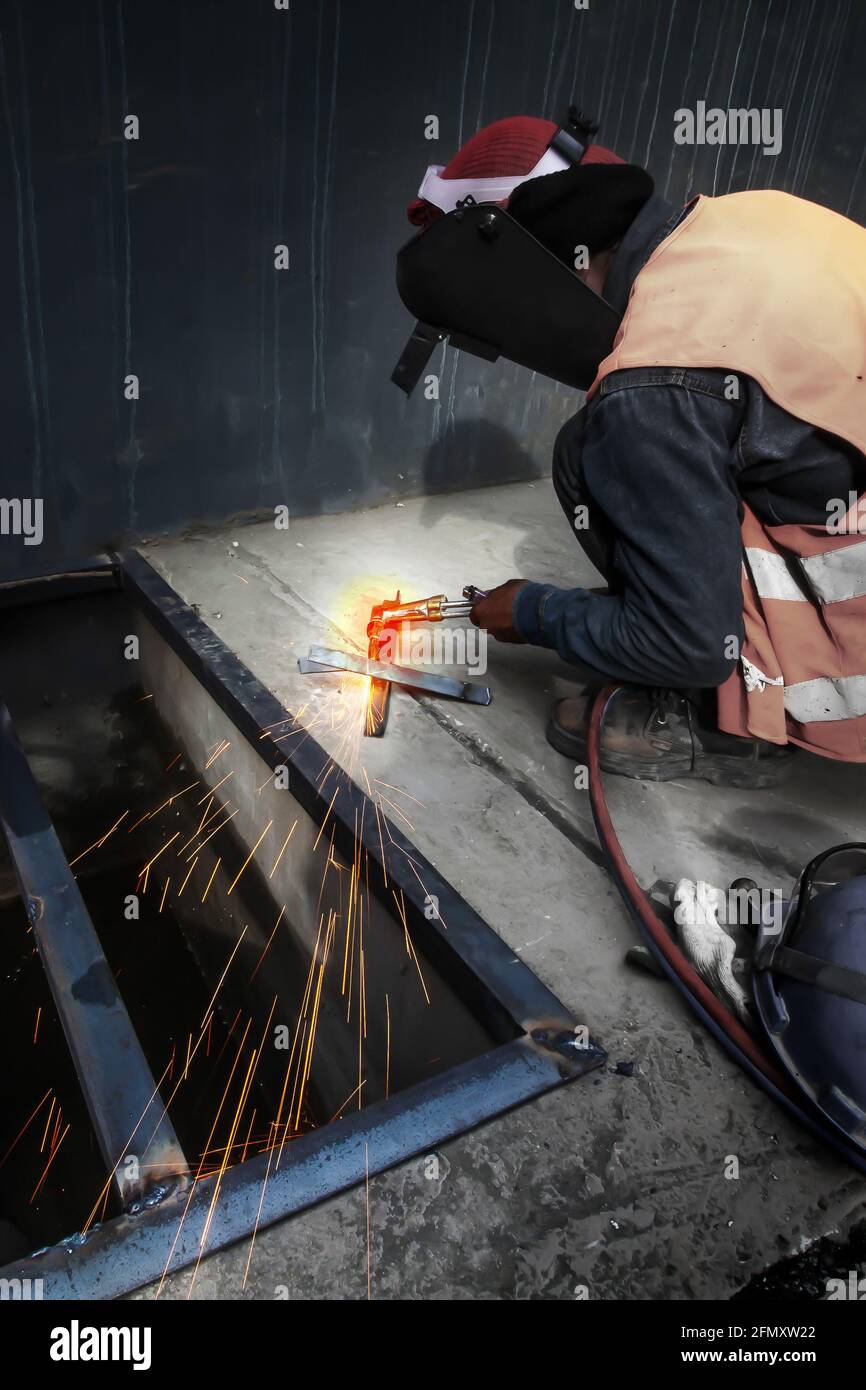 Asian man welding a metal grate, arc welding process with sparks. Long exposure. Focus on sparkling. Stock Photo