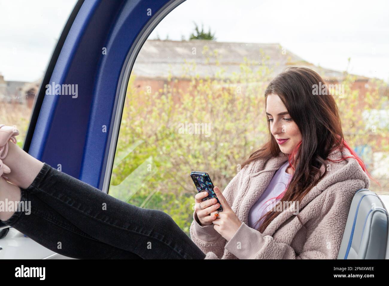 a young woman sitting at the front of double decker bus with her feet up and text messaging Stock Photo