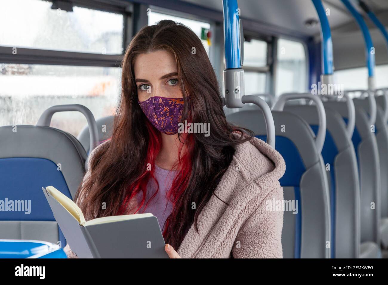 a woman sitting on a bus holding a book but looking to camera Stock Photo