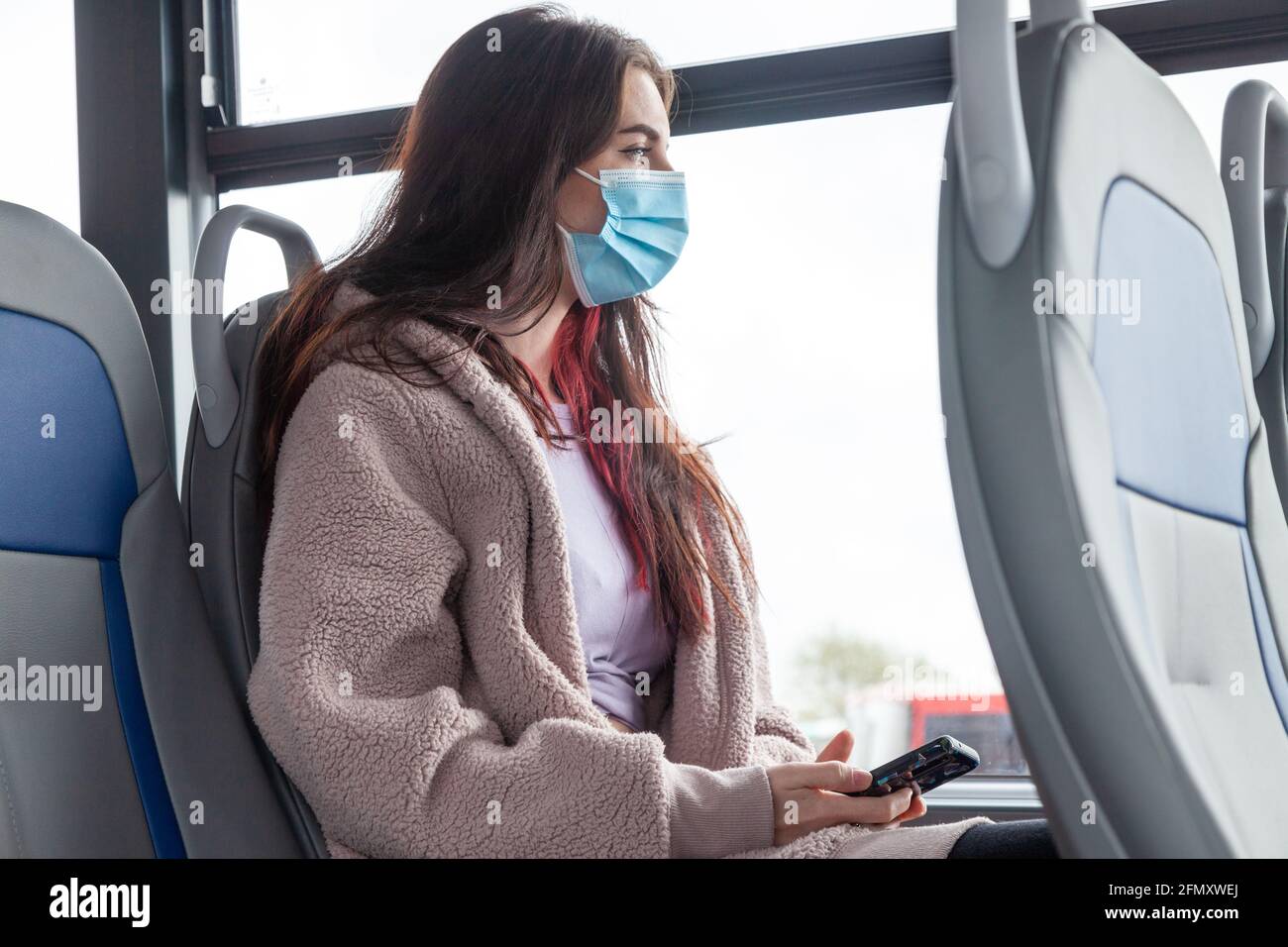 a woman wearing a face mask on a bus and looking out of the window
