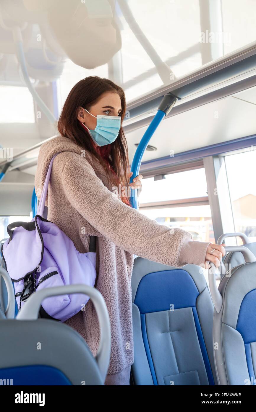 A young woman standing up inside of a bus wearing a face mask Stock