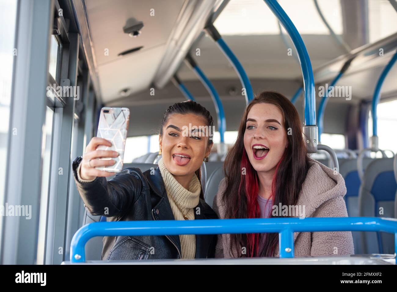 Two young women pulling faces and taking a selfie of themselves inside a bus Stock Photo