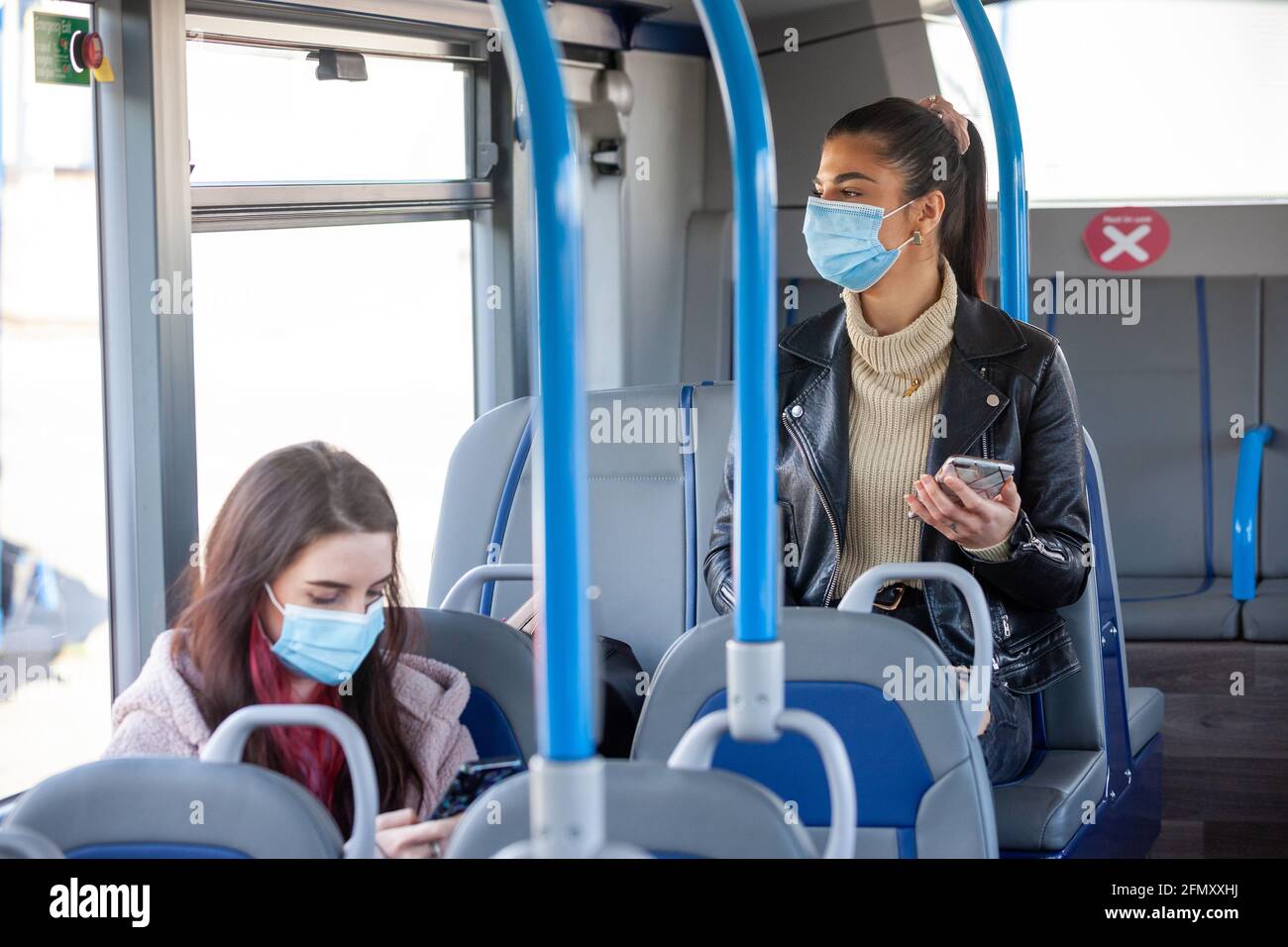 Two women in their twenty's travelling on a bus wearing face masks