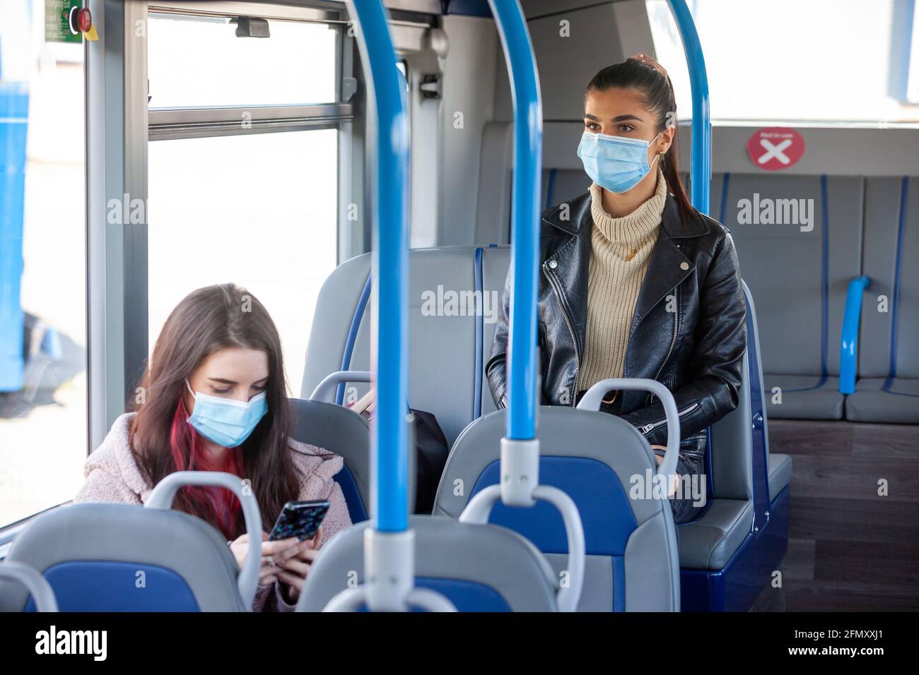 Two women in their twenty's travelling on a bus wearing face masks