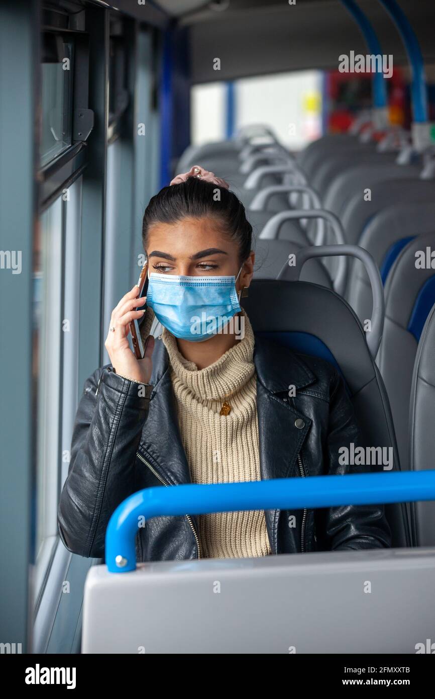 Woman travelling on a bus wearing a face mask and talking on a mobile