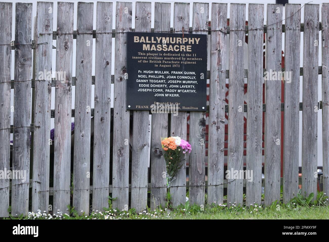 Flowers left below a plaque to commemorate the Ballymurphy massacre on