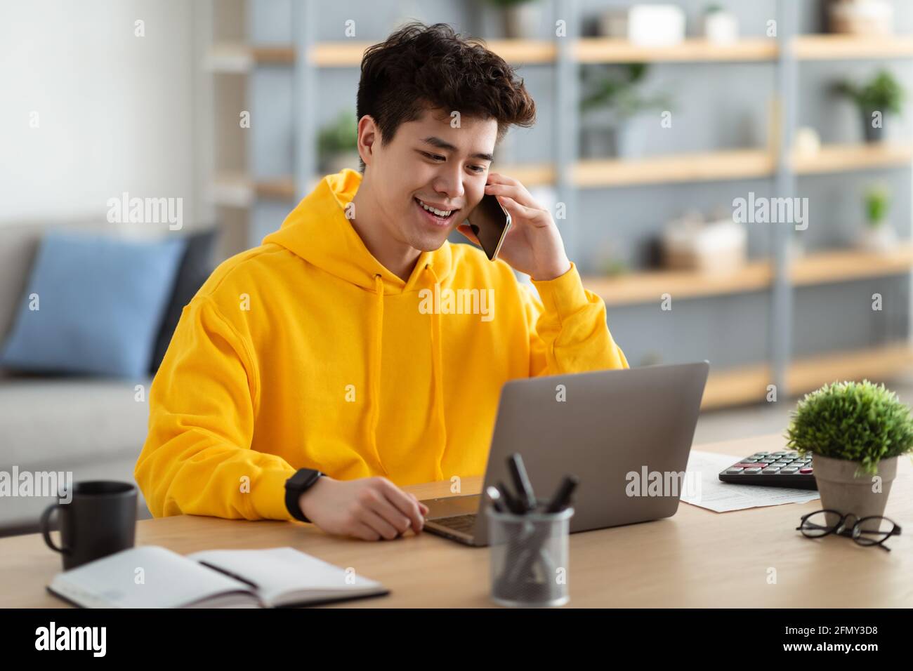 Smiling asian man working and talking on phone at home Stock Photo