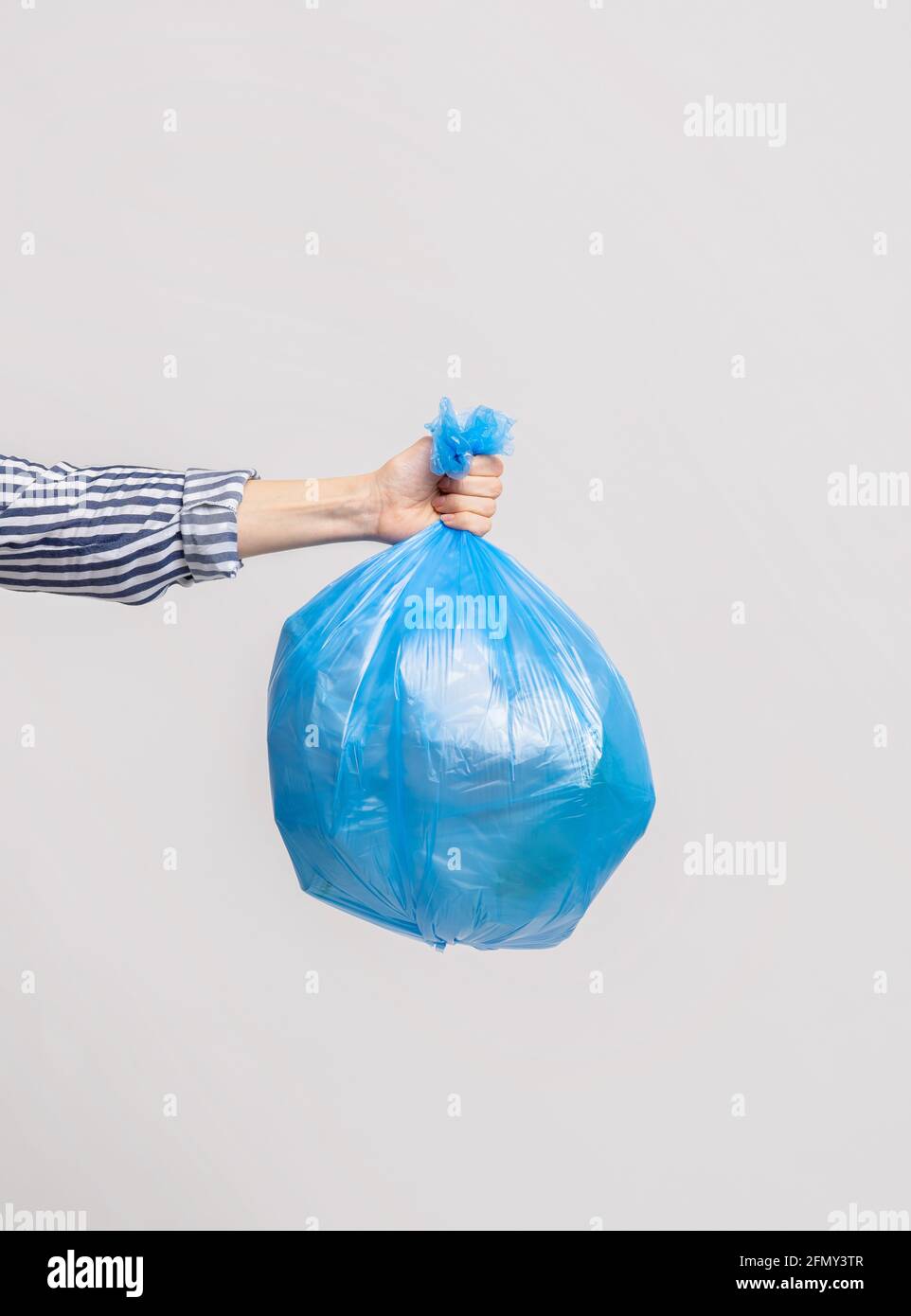 https://c8.alamy.com/comp/2FMY3TR/female-hand-holding-blue-plastic-bag-with-garbage-over-light-grey-background-2FMY3TR.jpg