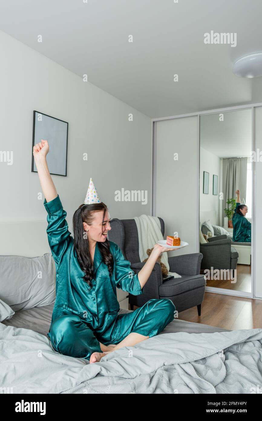 Young woman sits the bed her pajamas and holds a cake and screams with joy. Wellness concept. Rest at home Stock Photo