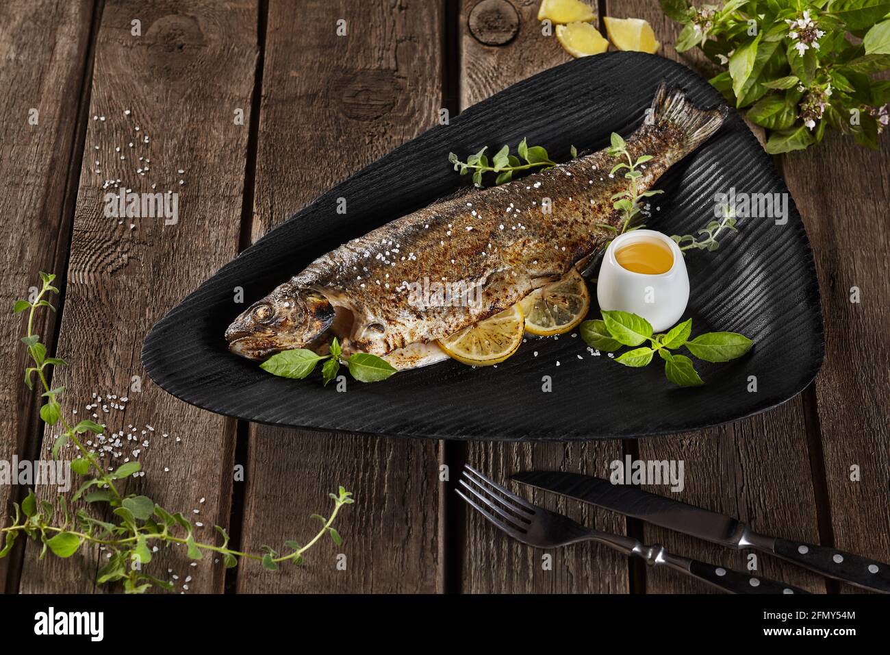 Grilled rainbow trout with lemon and herbs on wooden table Stock Photo