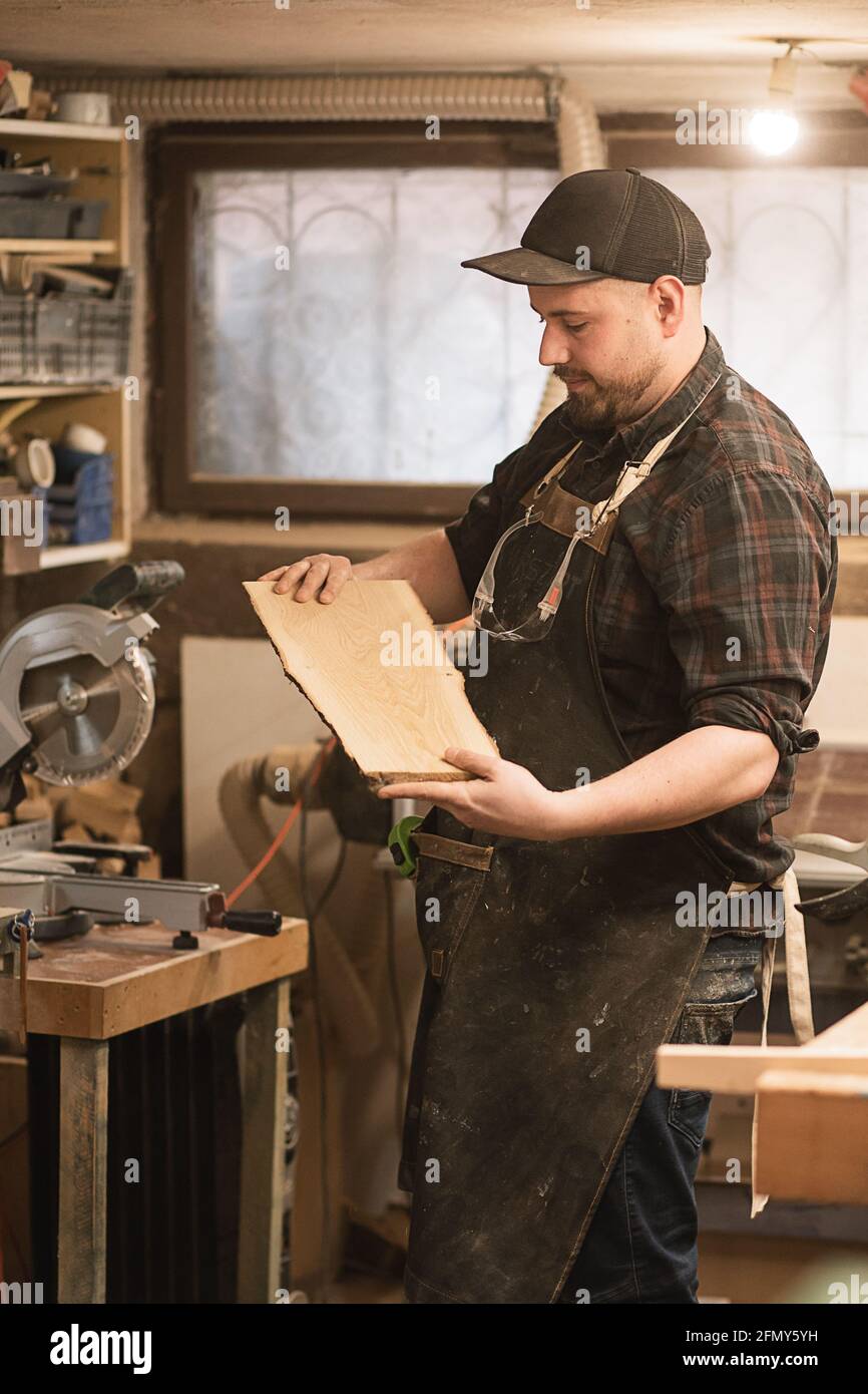 A carpenter holds piece of wood in his hands in workshop Stock Photo