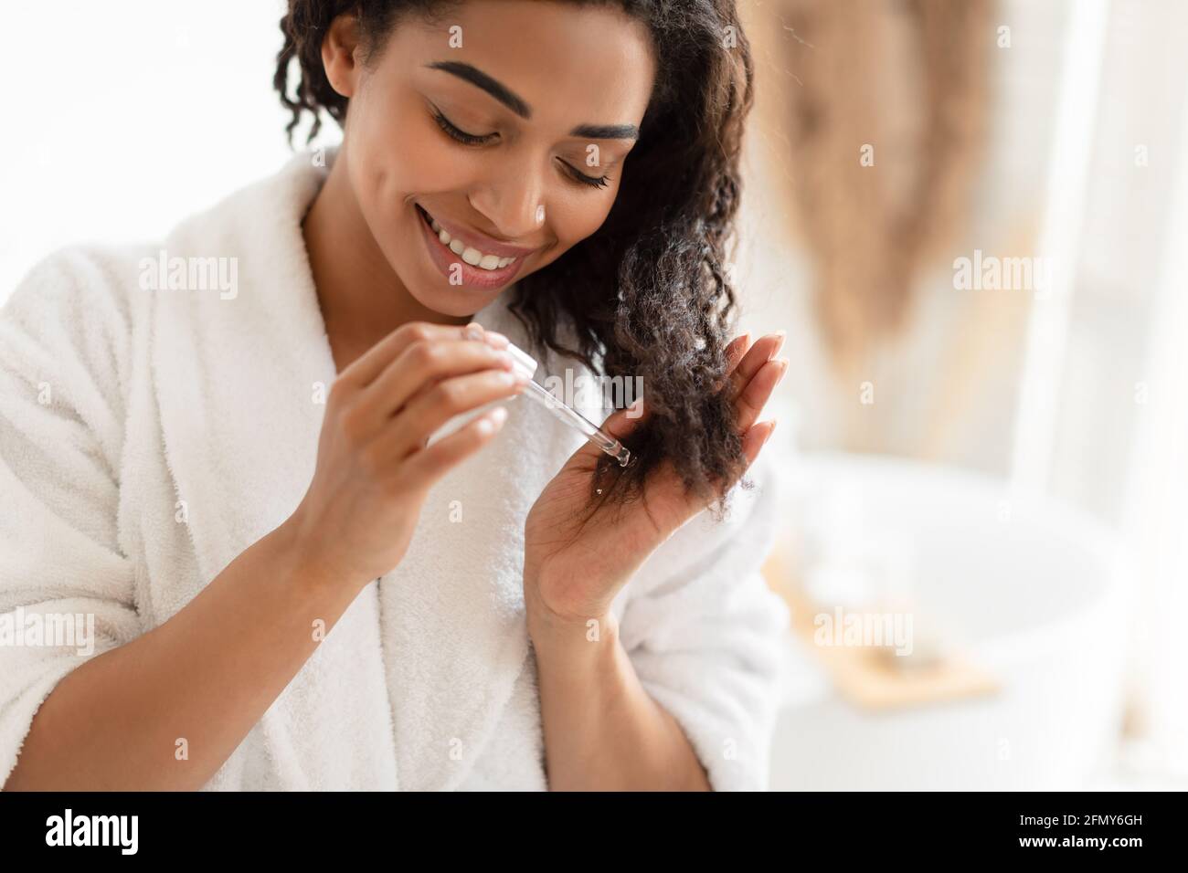 African American Woman Applying Serum On Damaged Hair In Bathroom Stock ...