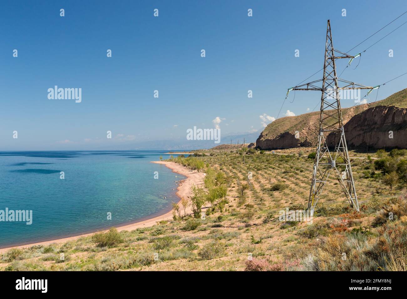 The southern shore of the Issyk Kul lake. Kyrgyzstan. The power line runs near the lake. Electricity pylon Stock Photo