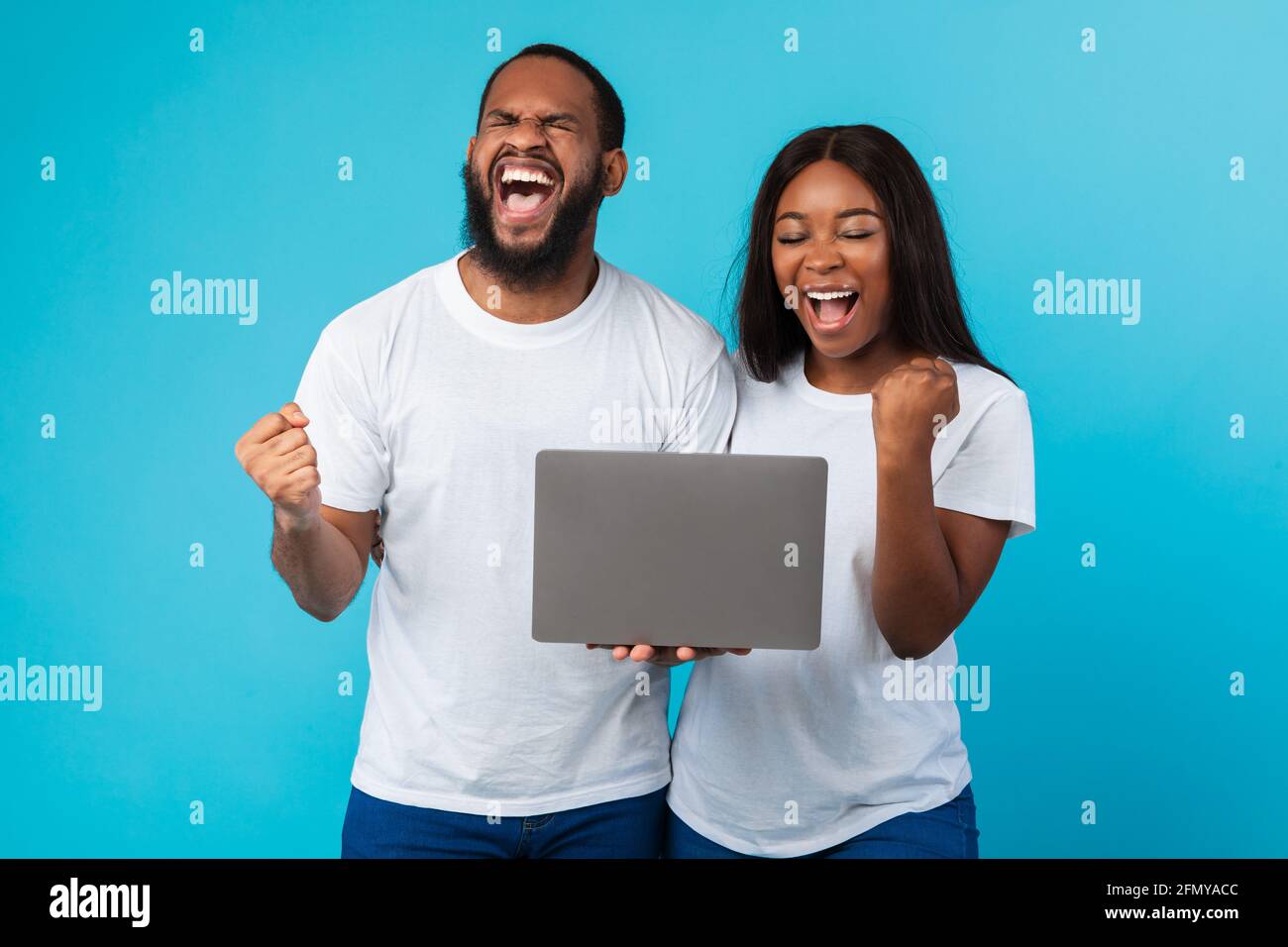 Black couple using laptop celebrating success shaking fists Stock Photo ...