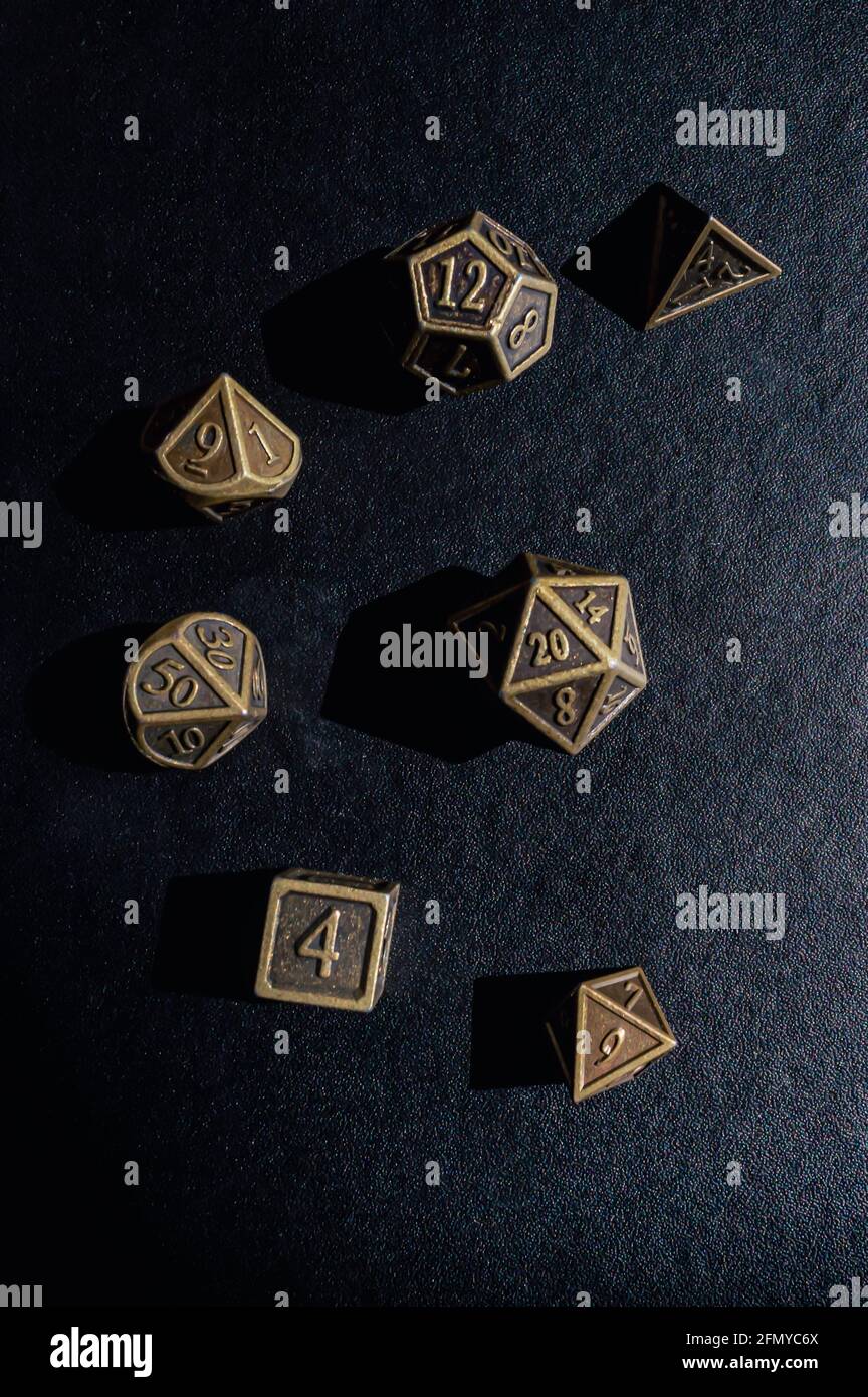 Vertical image of a set of bronze metal role-playing game dice on a black surface Stock Photo