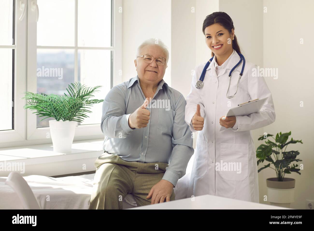 Portrait of happy satisfied senior man and young doctor giving thumbs up together Stock Photo