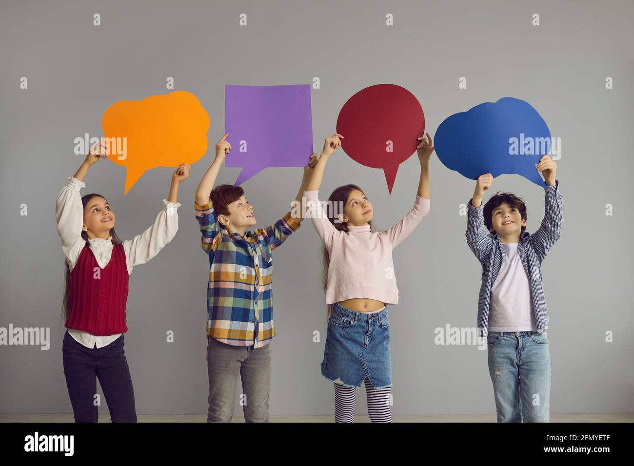 Group of happy little kids standing in studio and holding up multicolored speech bubbles Stock Photo