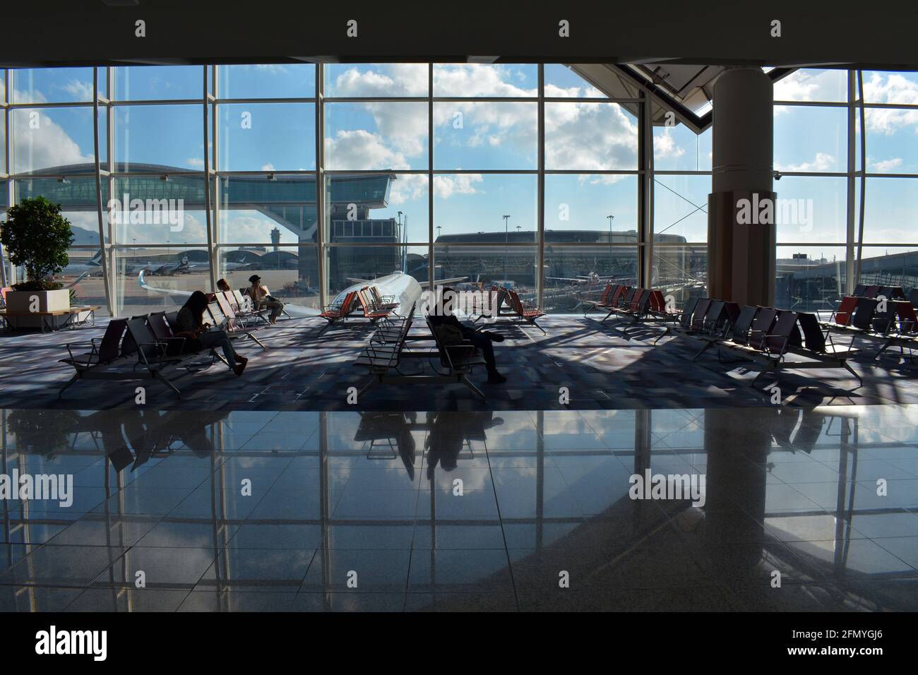 A few passengers wait for their flight in front of a huge window offering views of Chek Lap Kok, Hong Kong international airport. Stock Photo