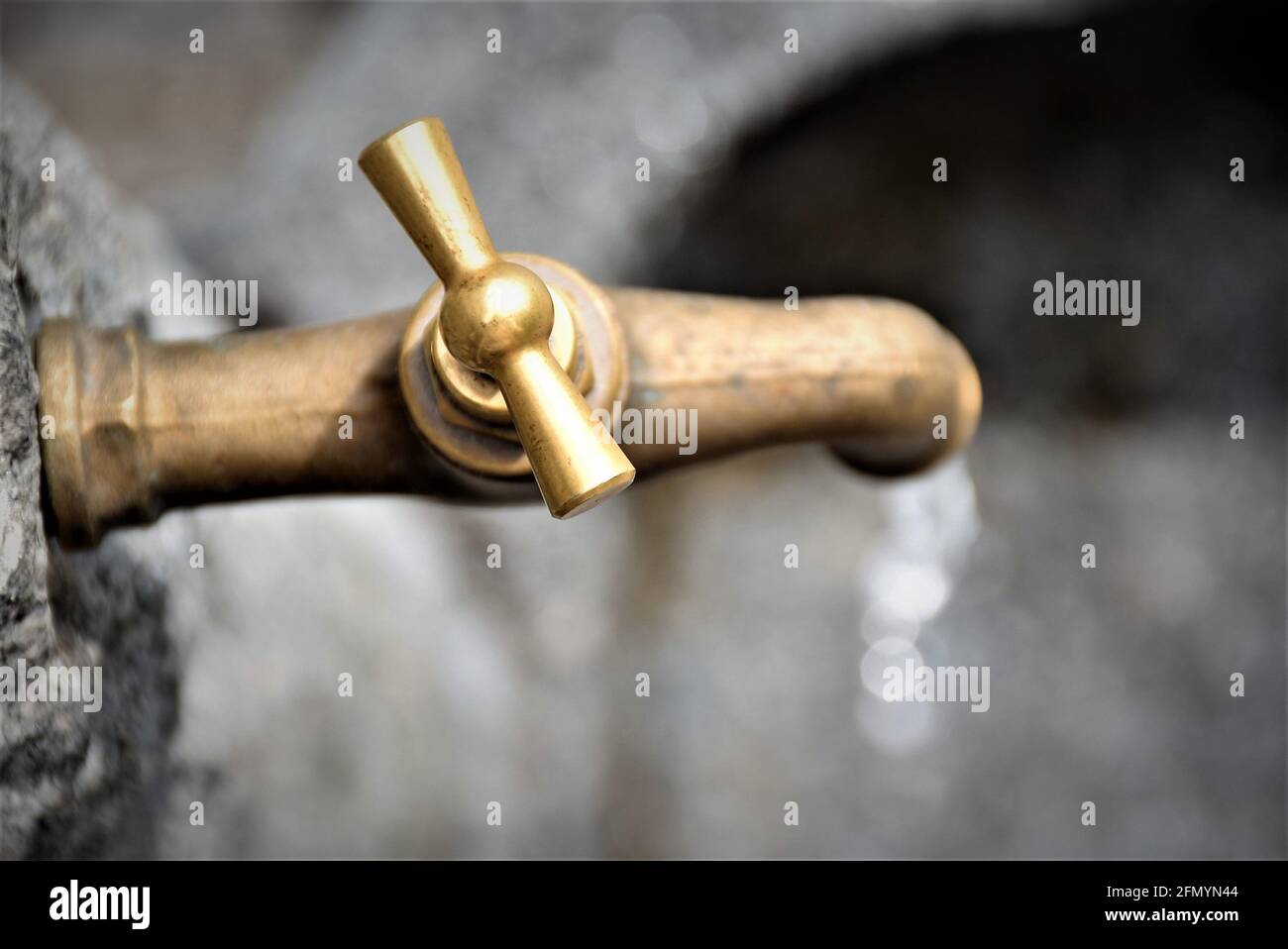 Top view of an old water tap. The brass faucet is shining brightly in the sun. Running water looks fresh. The drops have a nice bokey. Vintage. Rustic. Stock Photo