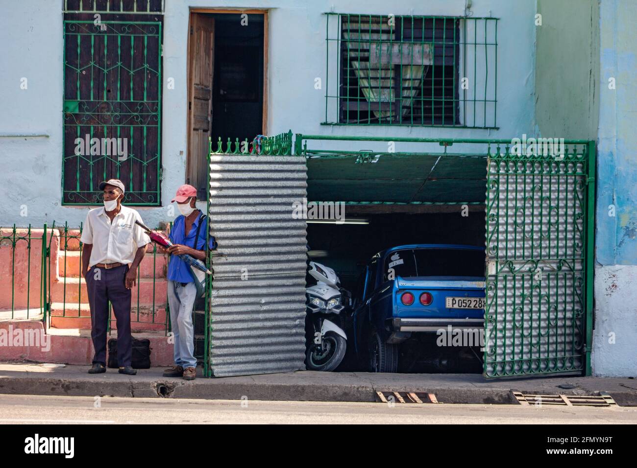 Two Cuban men wearing face mask by an open garage door in Santiago de Cuba, Cuba. It is the time of the Covid-19 pandemic Stock Photo