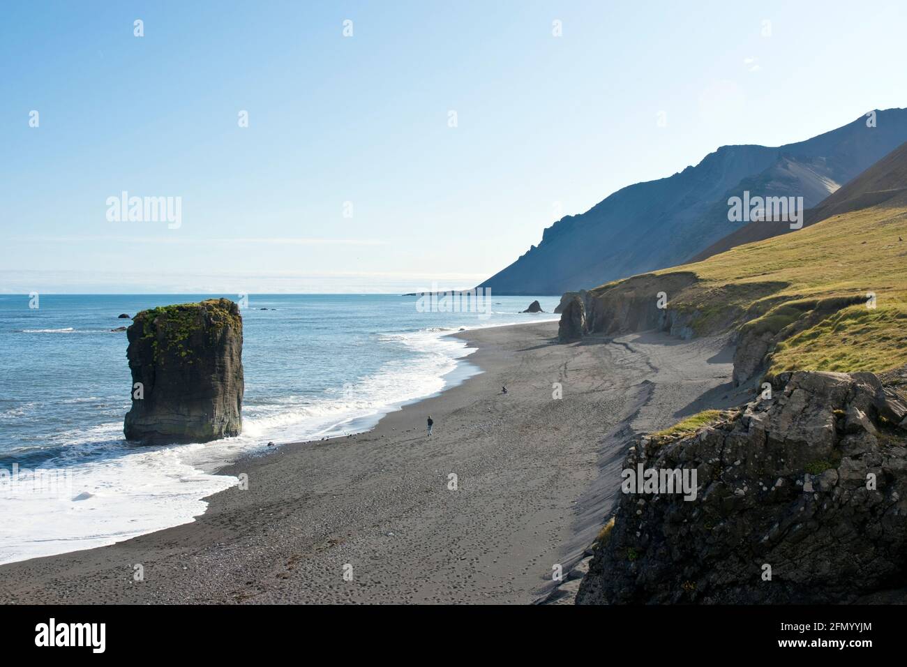 People walk on the black sand beach, along the cliffs and rock formations at Fauskasandur in east Iceland. Stock Photo