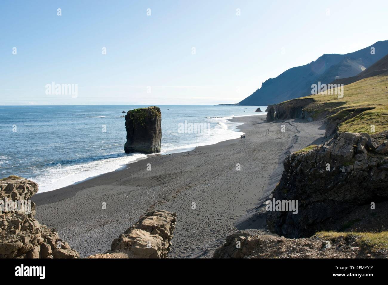 People walk on the black sand beach, along the cliffs and rock formations at Fauskasandur in east Iceland. Stock Photo