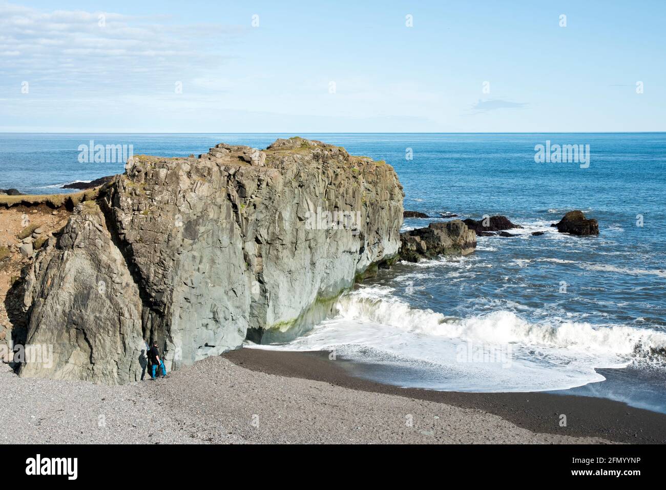 Father and son climb on the rock formations at Fauskasandur, a black sand beach, in east Iceland. Stock Photo