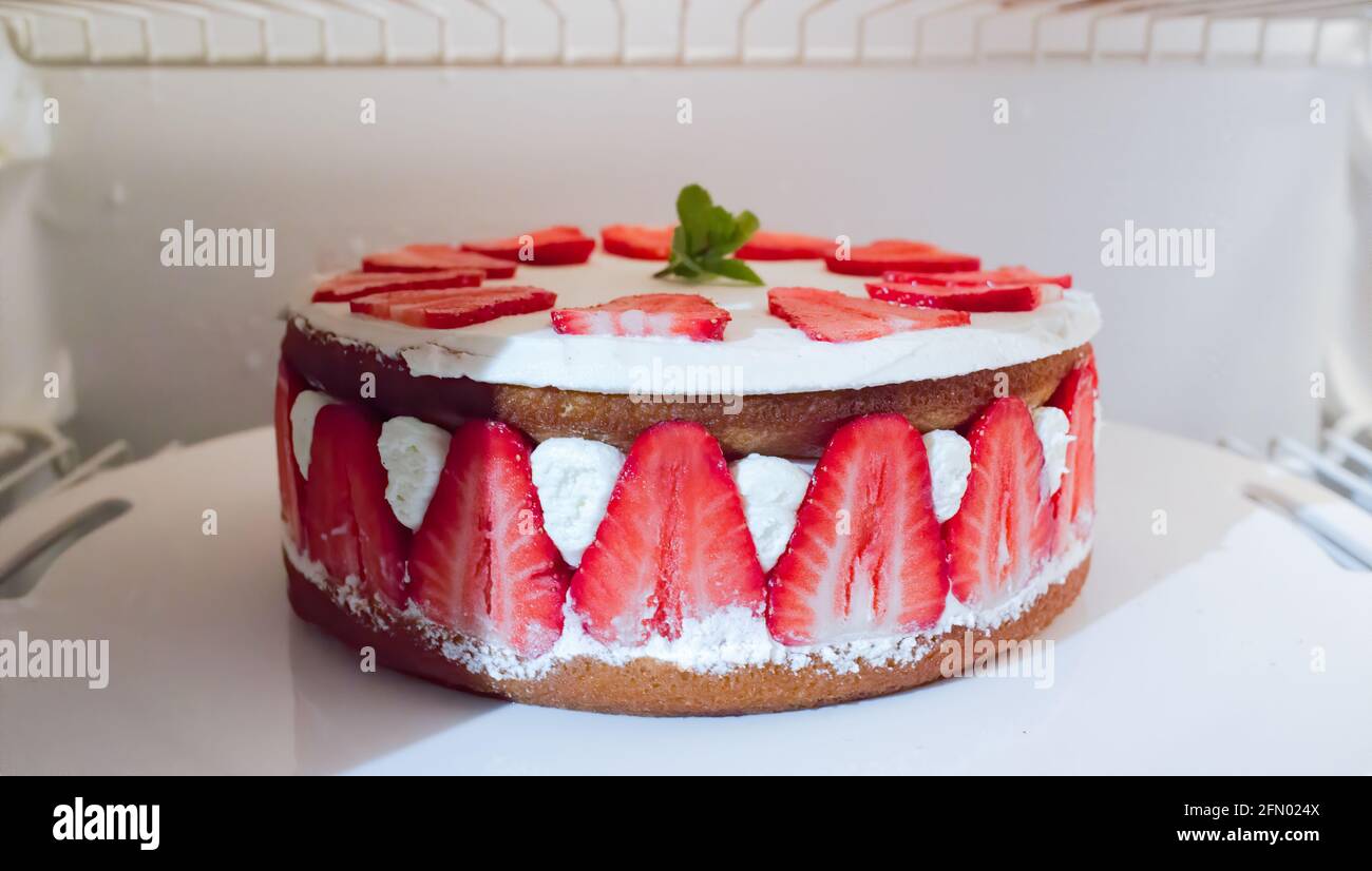 Strawberry and cream cake with fresh mint leaf on top in a refrigerator Stock Photo