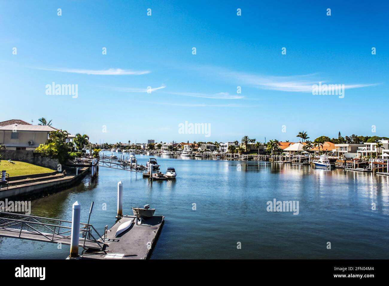 Canal in tropical setting with boat docks and moored boats by each waterside house and palm trees under blue sky Stock Photo