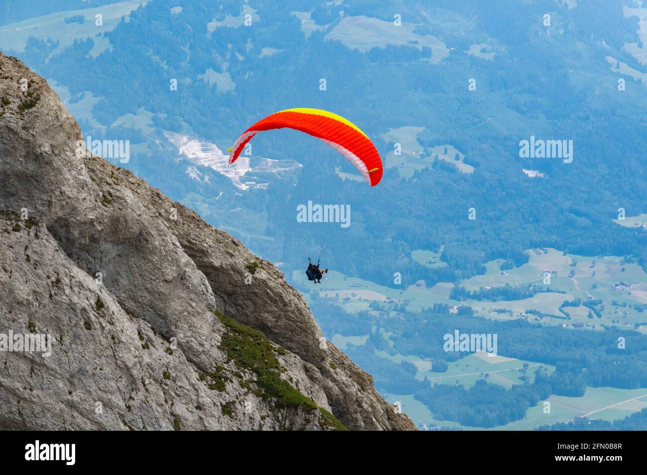 view Skydiving - parachute sport in the Alps at a mountain in sunny day with blue sky and clouds in springtime. Stock Photo
